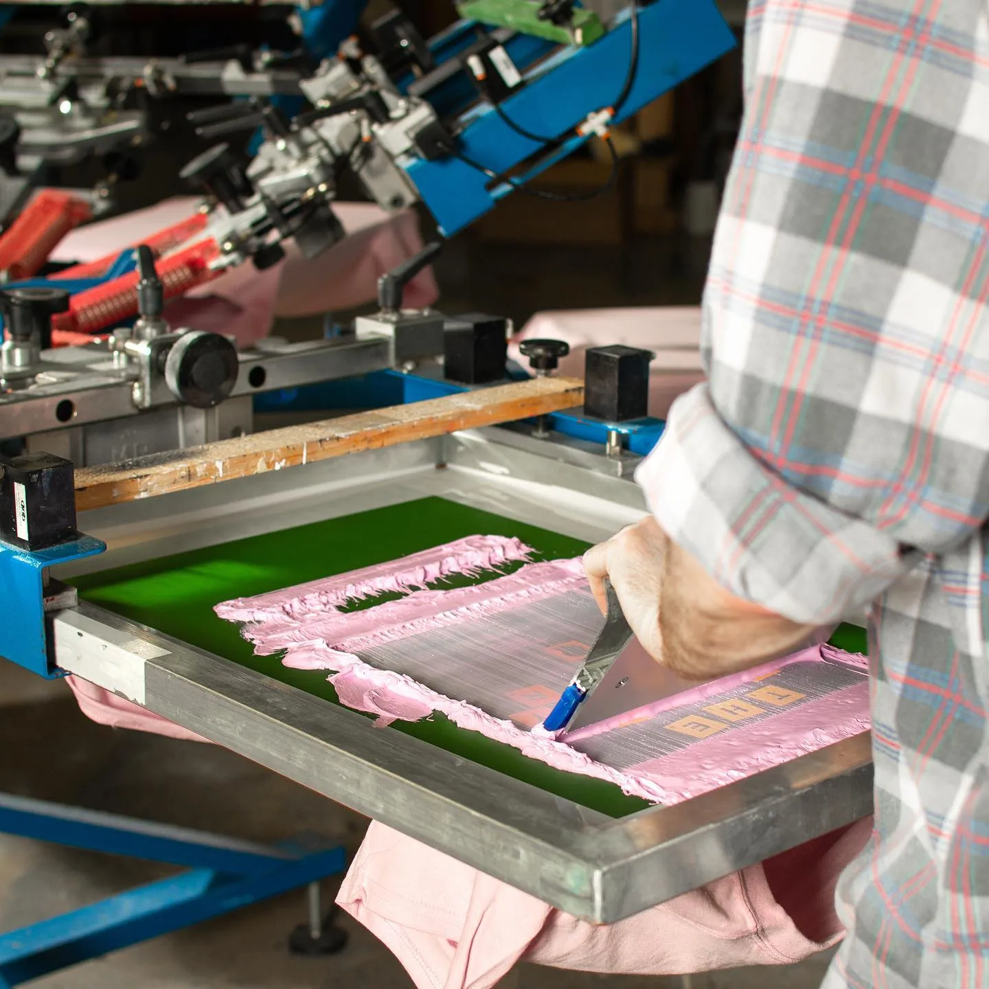Close-up of screen printing process with pink ink applied to T-shirt in small workshop — Whaleoni custom apparel production